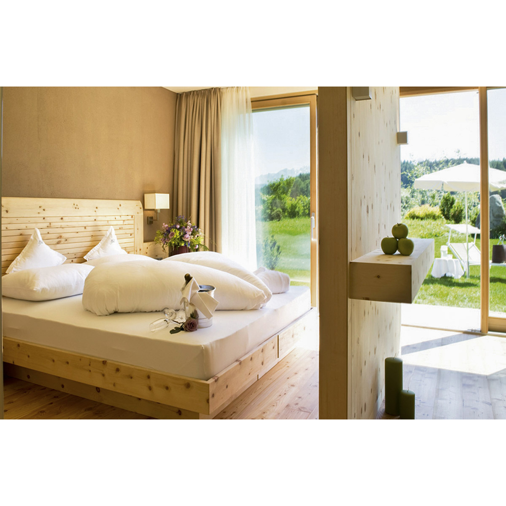 Ein helles Holzschlafzimmer mit großem Bett, Blumen und Blick auf eine grüne Wiese mit Sonnenschirm.