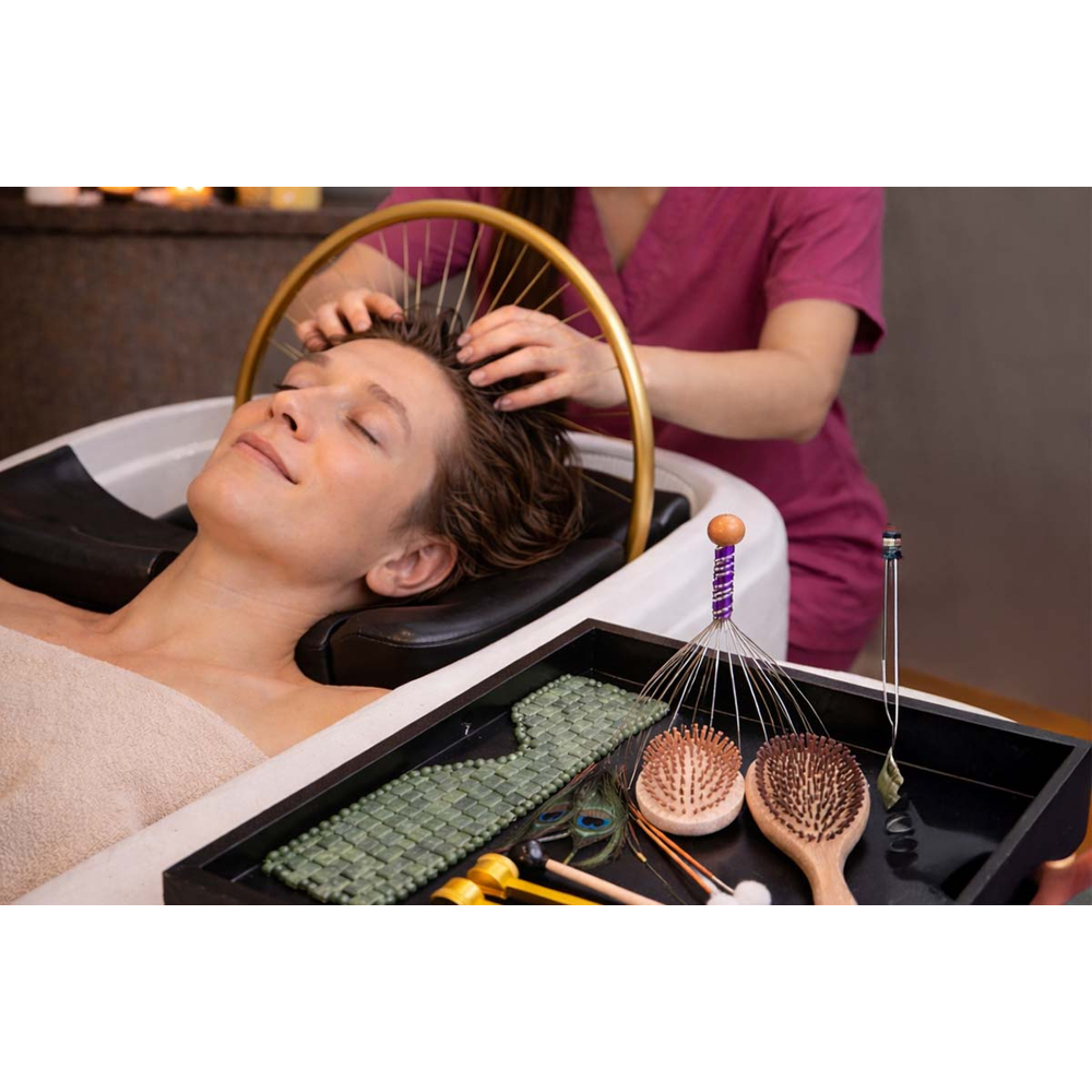 Eine Frau genießt eine Kopfmassage am Waschbecken mit Wellness-Utensilien im Vordergrund.