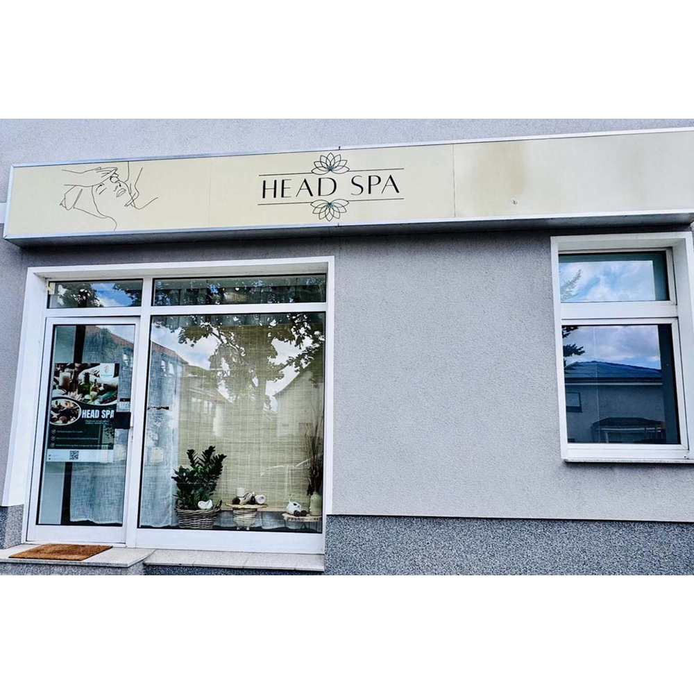 Außenansicht eines Head-Spa-Ladens mit weißem Schild, Glastür und Schaufenster mit Pflanzen und Bambusrollos.