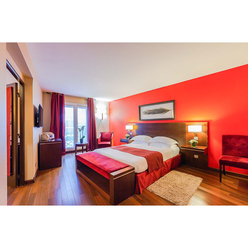 Hotelzimmer mit großem Bett, heller roter Wand, Holzfußboden und Sesseln.