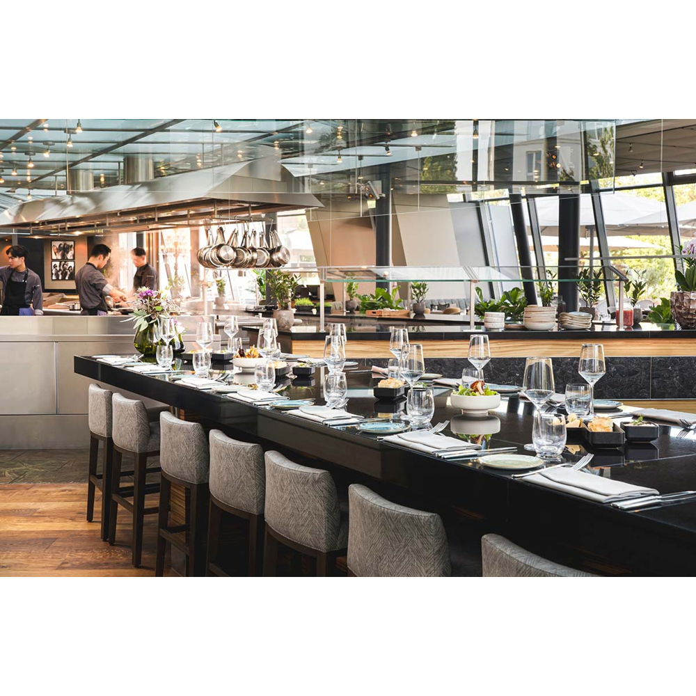 Moderne Restaurantküche mit einer langen schwarzen Bar und gepolsterten Barhockern im Vordergrund.