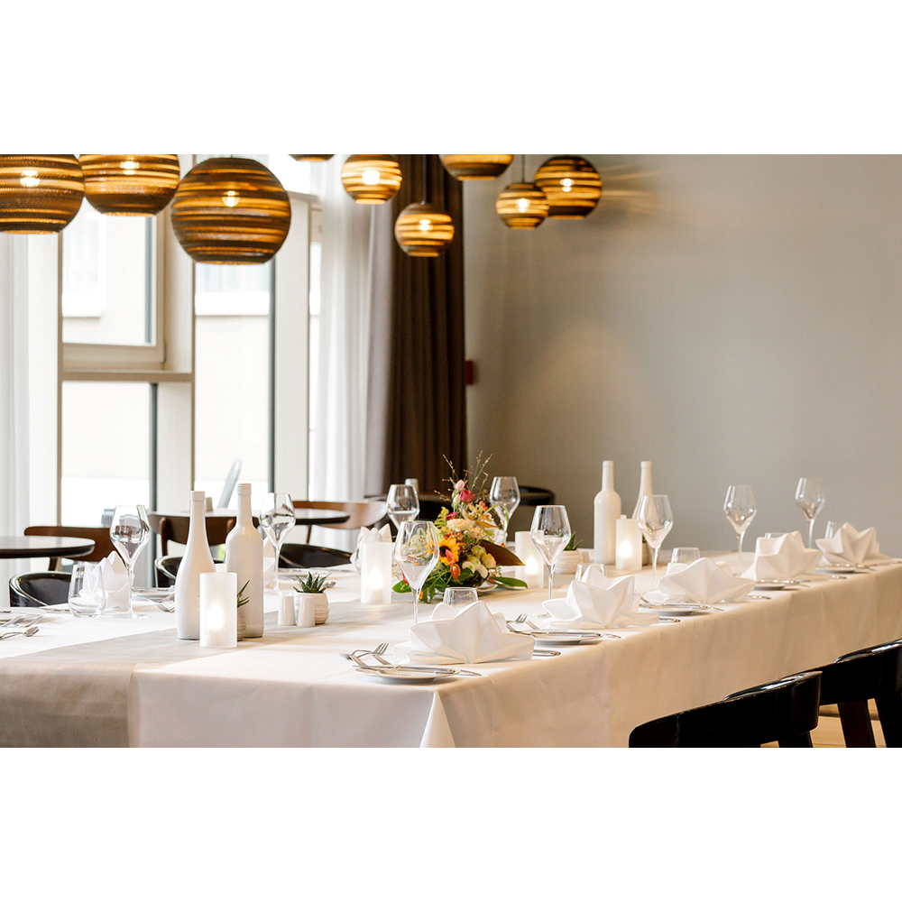 Ein elegant gedeckter langer Tisch in einem hellen Raum mit modernen Hängeleuchten und Blumenarrangement.