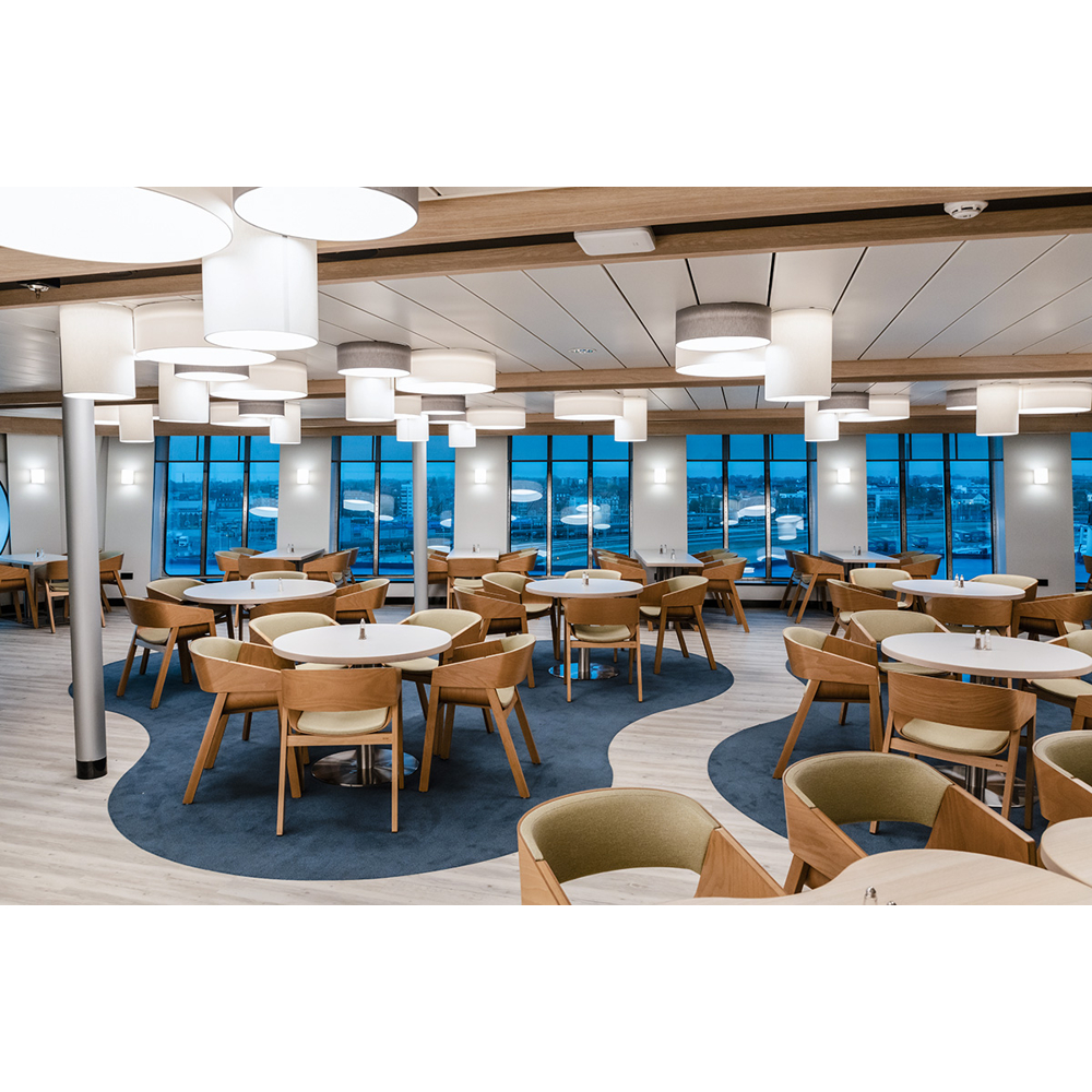 Ein modernes Restaurantinterieur mit runden Tischen, Holzstühlen, blauen Teppichen und großen Fenstern mit Stadtblick.