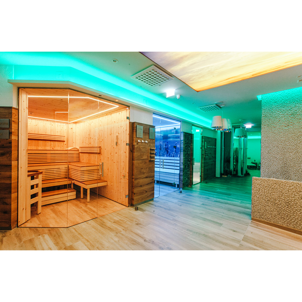 Ein moderner Wellnessbereich mit Holzs Sauna, Glastüren und stimmungsvoller grüner Beleuchtung auf Holzboden.
