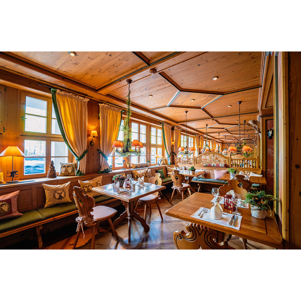 Gemütliches, holzgetäfeltes Alpin-Restaurant mit gedeckten Tischen, grünen Kissen und warmem Licht.