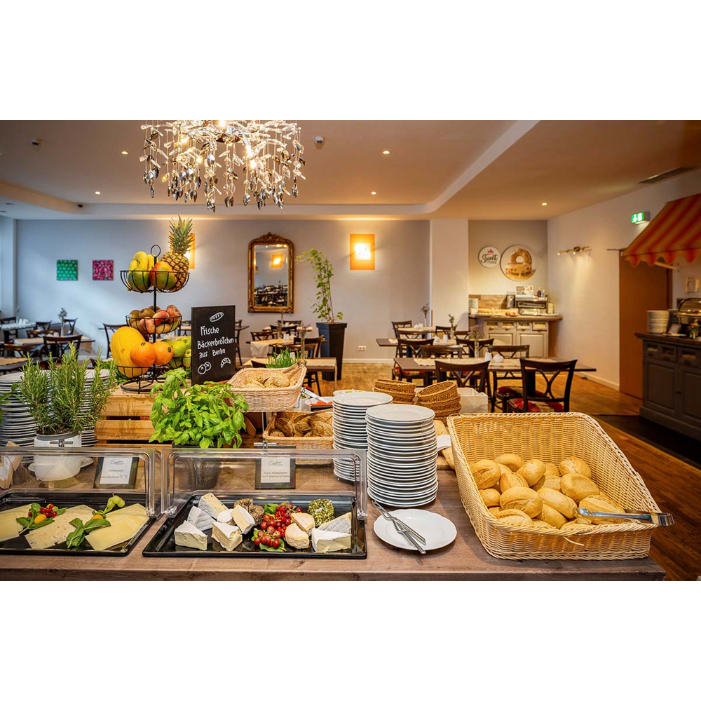 Frühstücksbüfett mit Käse, Obst, Brötchen und Tellern in einem Restaurant.