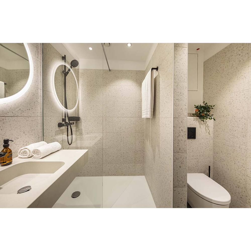 Ein modernes Bad mit Waschbecken, Glasdusche mit schwarzen Armaturen und separater Toilette an beigen Fliesenwänden.