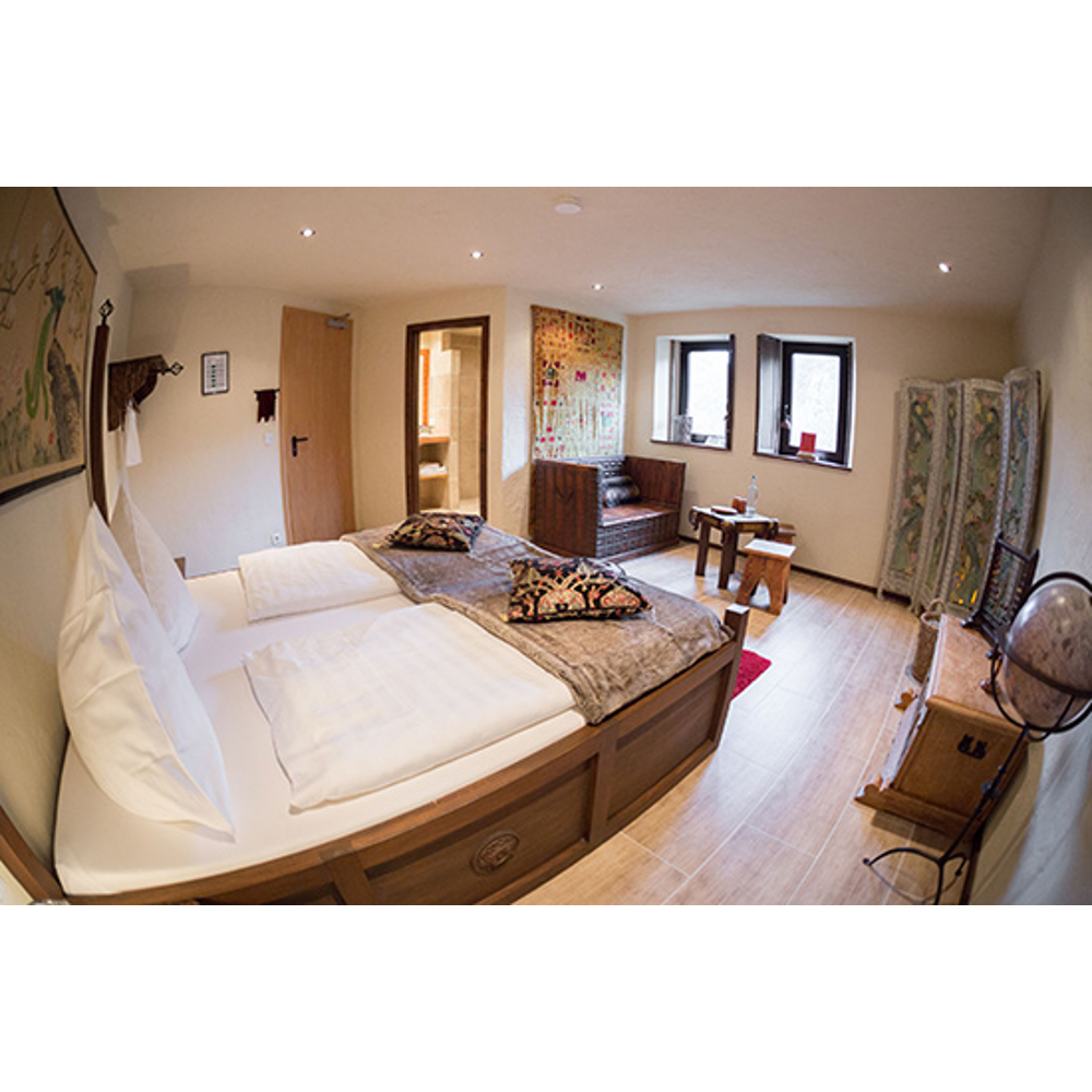 Gemütliches Schlafzimmer mit großem Holzbett, heller Bettwäsche, zwei Fenstern, Kommode und asiatischer Wandkunst.