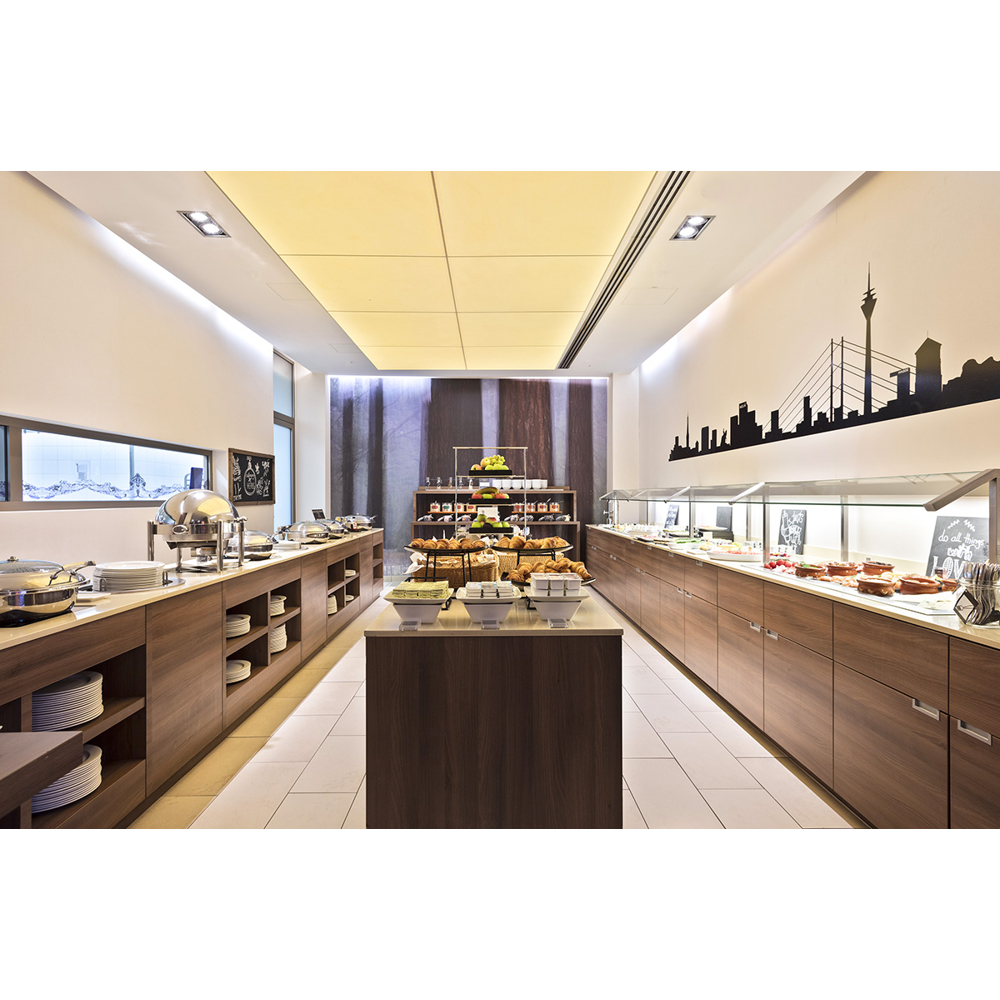 Moderne Hotellobby mit Frühstücksbuffet, Holztischen und einer Stadtsilhouette an der Wand.