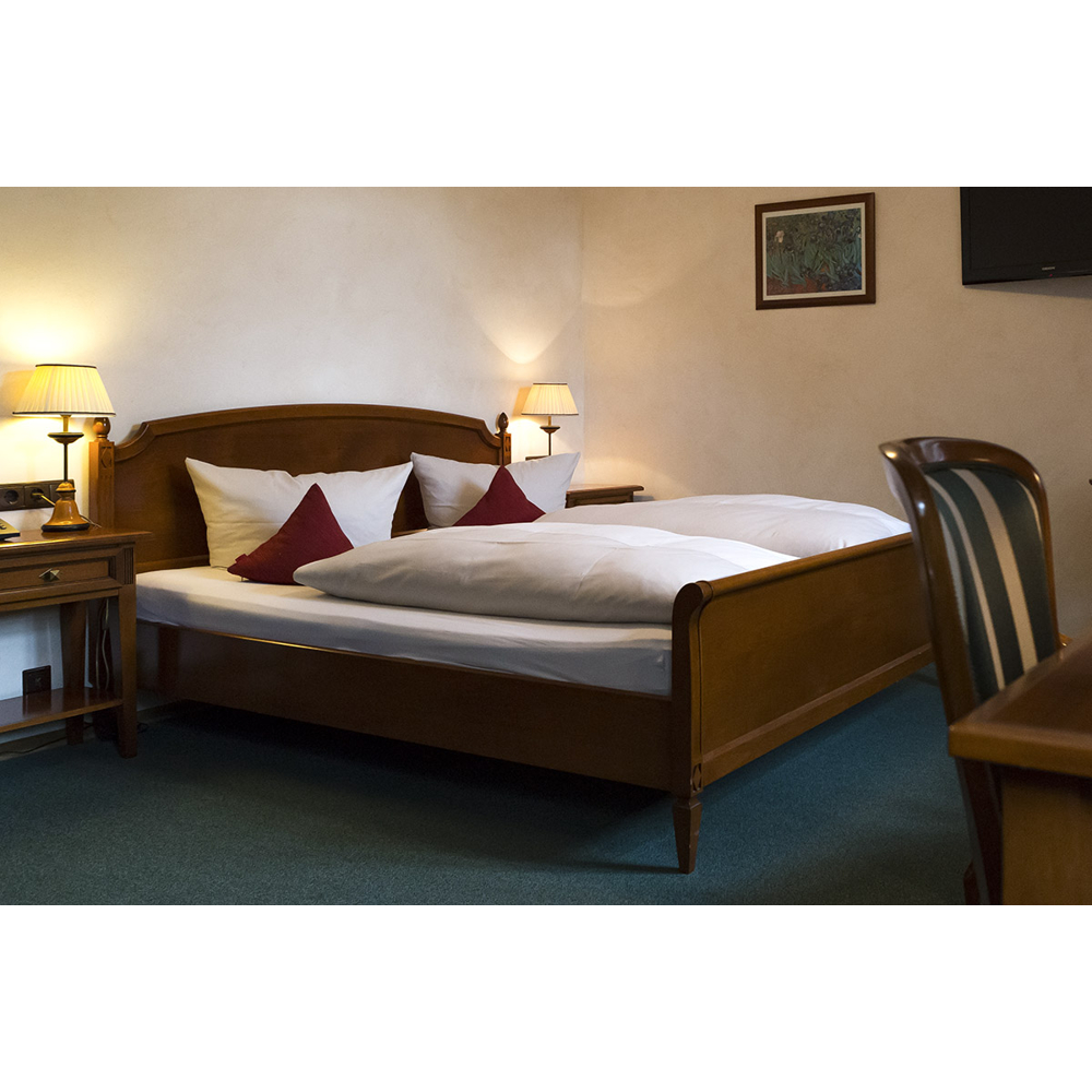 Ein gemütliches Schlafzimmer mit einem Holzbett, weißen Kissen, roten Akzentkissen, Nachttischlampen und einem blauen Teppich.