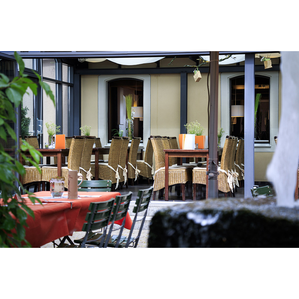 Gemütliche Restaurant-Terrasse mit Holztischen, Rattanstühlen und rot gedeckten Tischen im Vordergrund.
