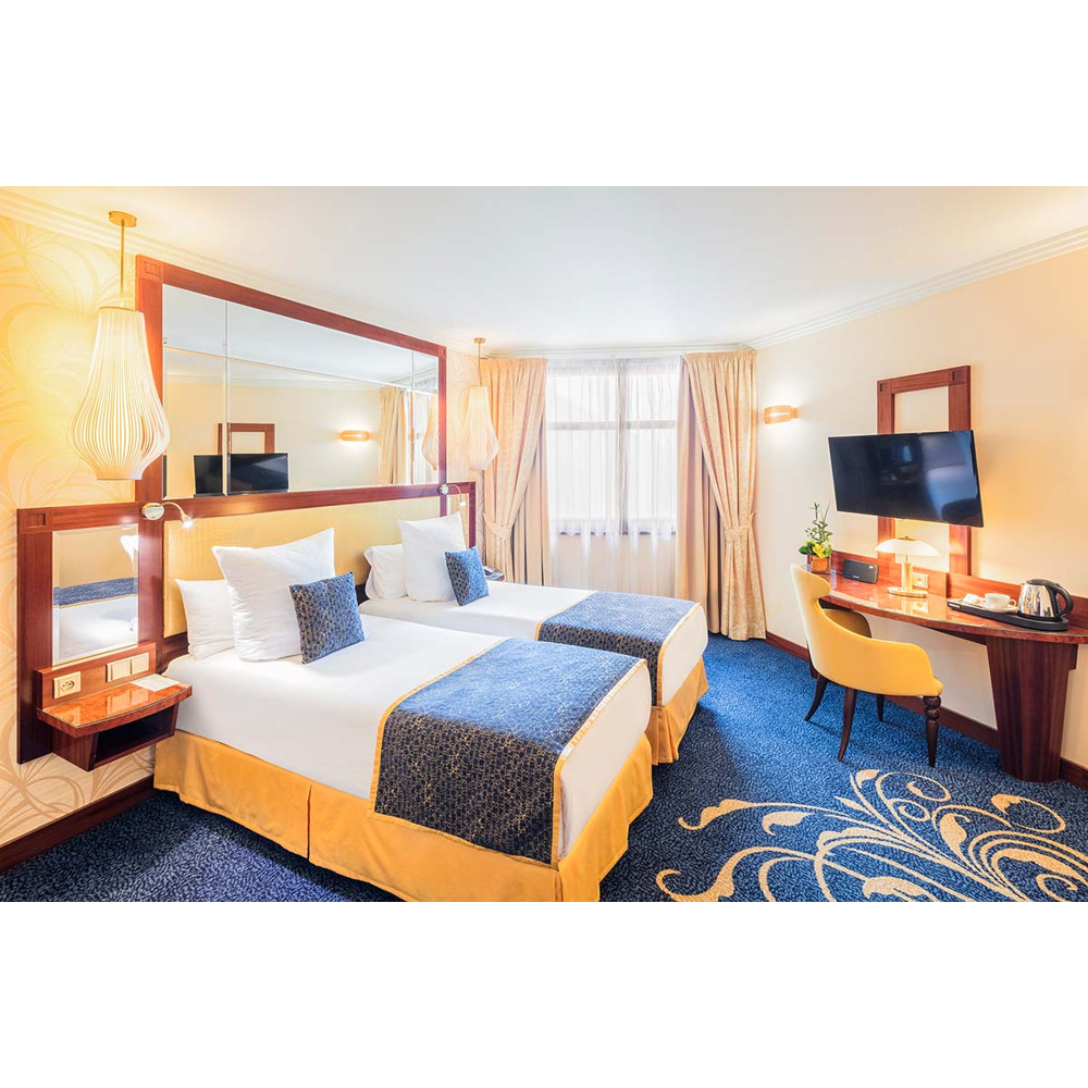 Ein Hotelzimmer mit zwei Einzelbetten, blauem Teppich, einem Schreibtisch mit gelbem Stuhl und TV.