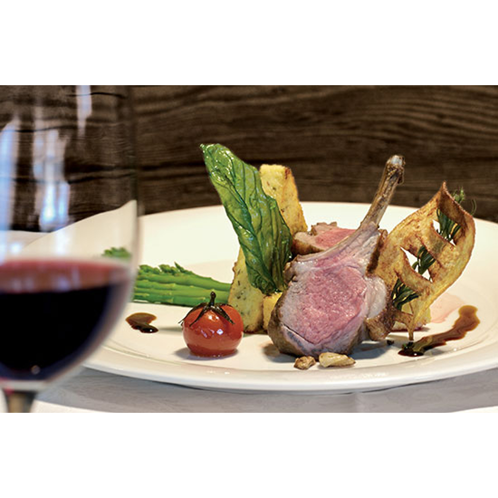 Lammkotelett mit Spargel, Kirschtomate und Kräutern auf weißem Teller, im Vordergrund ein Glas Rotwein.
