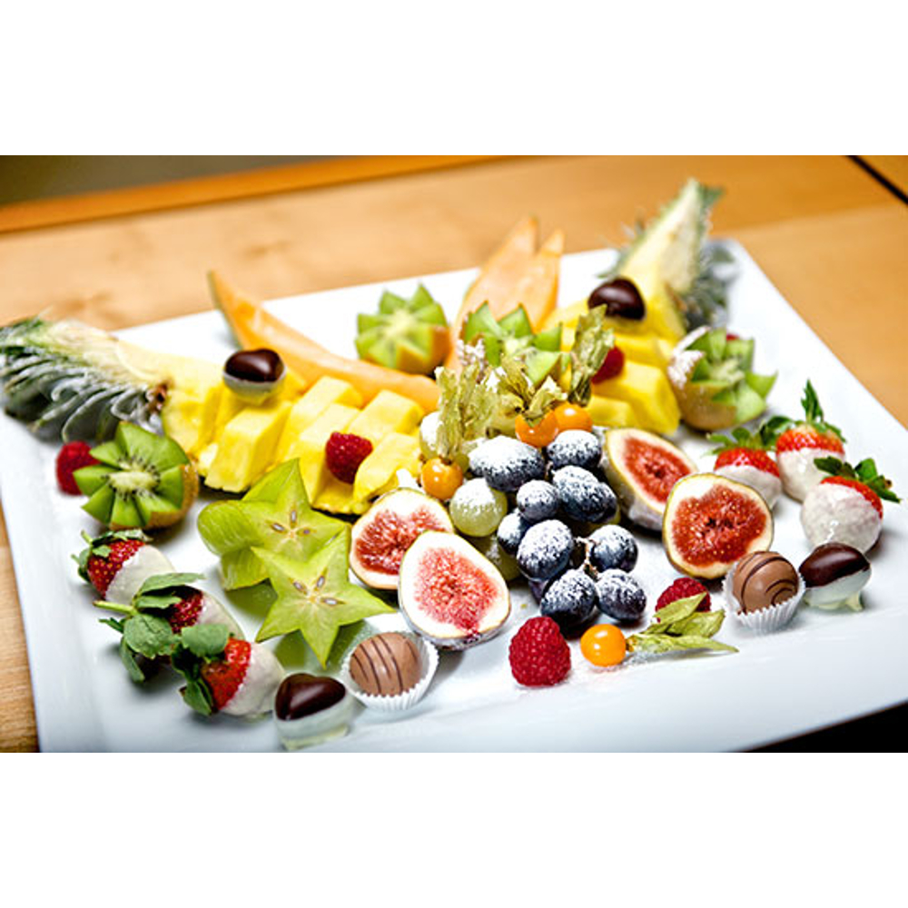 Eine bunte Platte mit aufgeschnittenem Obst wie Ananas, Kiwis, Feigen und Beeren, garniert mit Pralinen auf einem Teller.