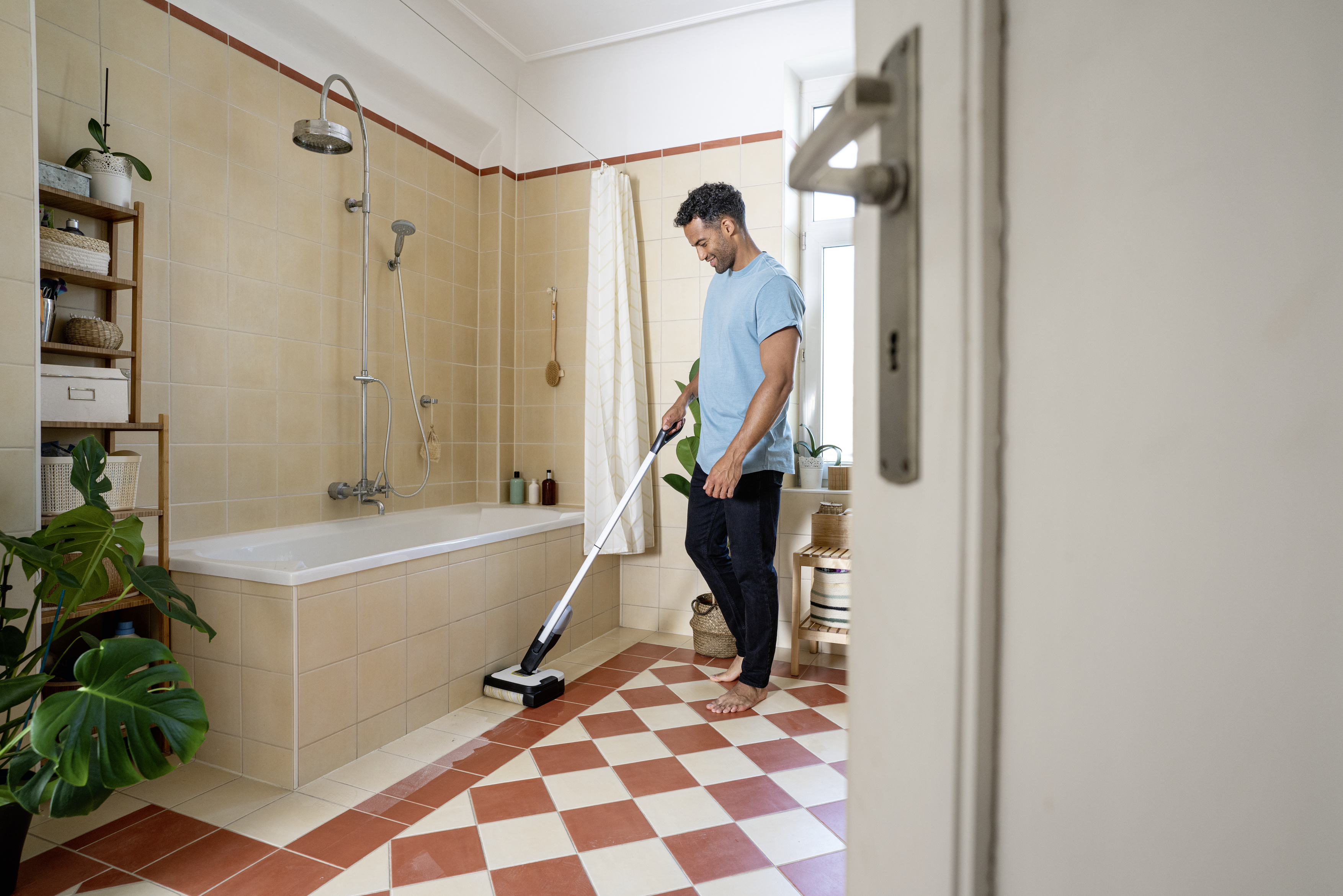 Un uomo pulisce il pavimento piastrellato rosso e bianco di un bagno piastrellato di beige con un lava pavimenti.
