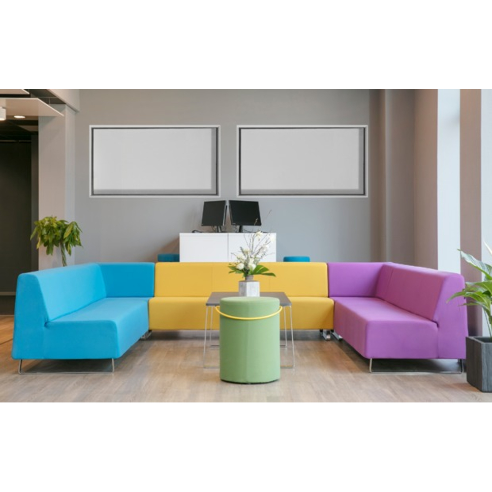 Moderne Lounge mit bunten Sofas in Blau, Gelb und Lila sowie einem grünen Hocker und Pflanzen.