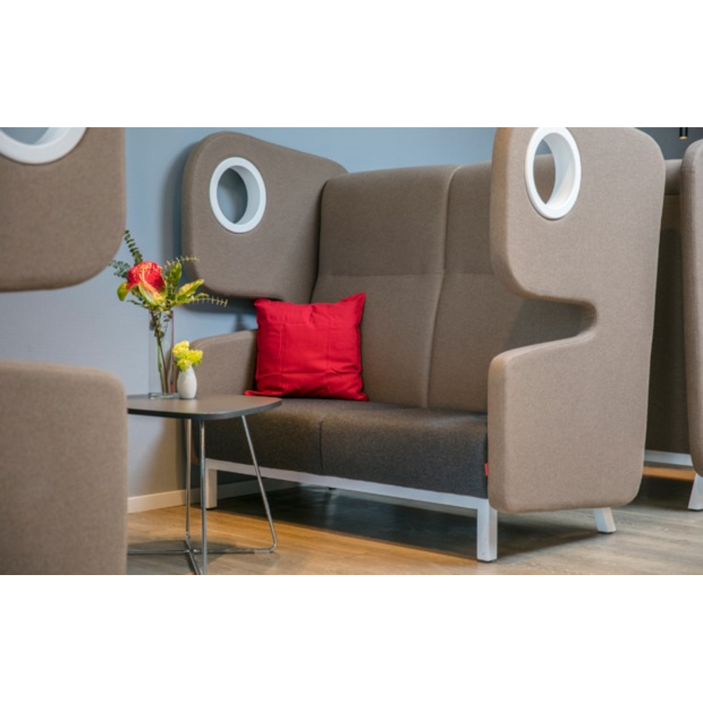 Ein graues Sofa mit hoher Rückenlehne und rotem Kissen steht neben einem kleinen Tisch mit Blumen.