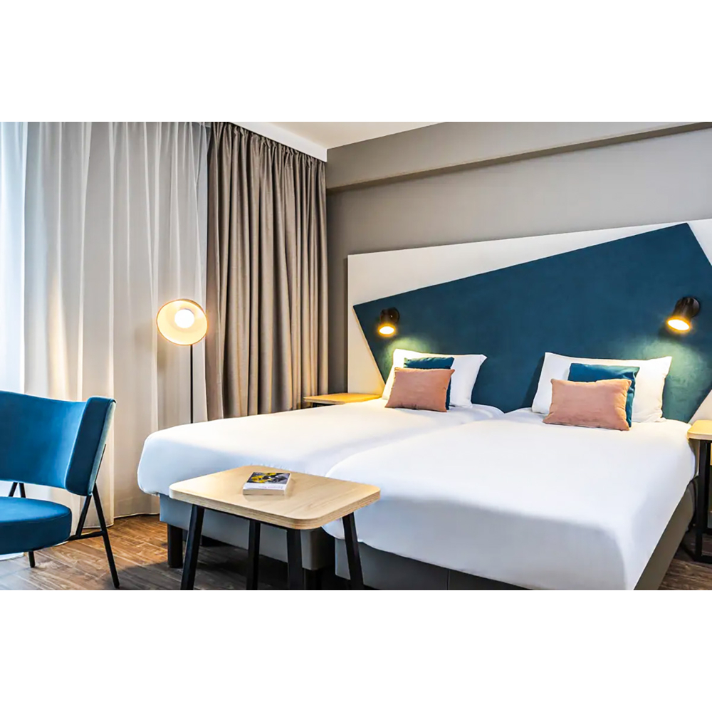 Moderne Hotelzimmer mit zwei Betten, einer blauen Wandverkleidung, Vorhängen, einem Sessel und Holztischen.