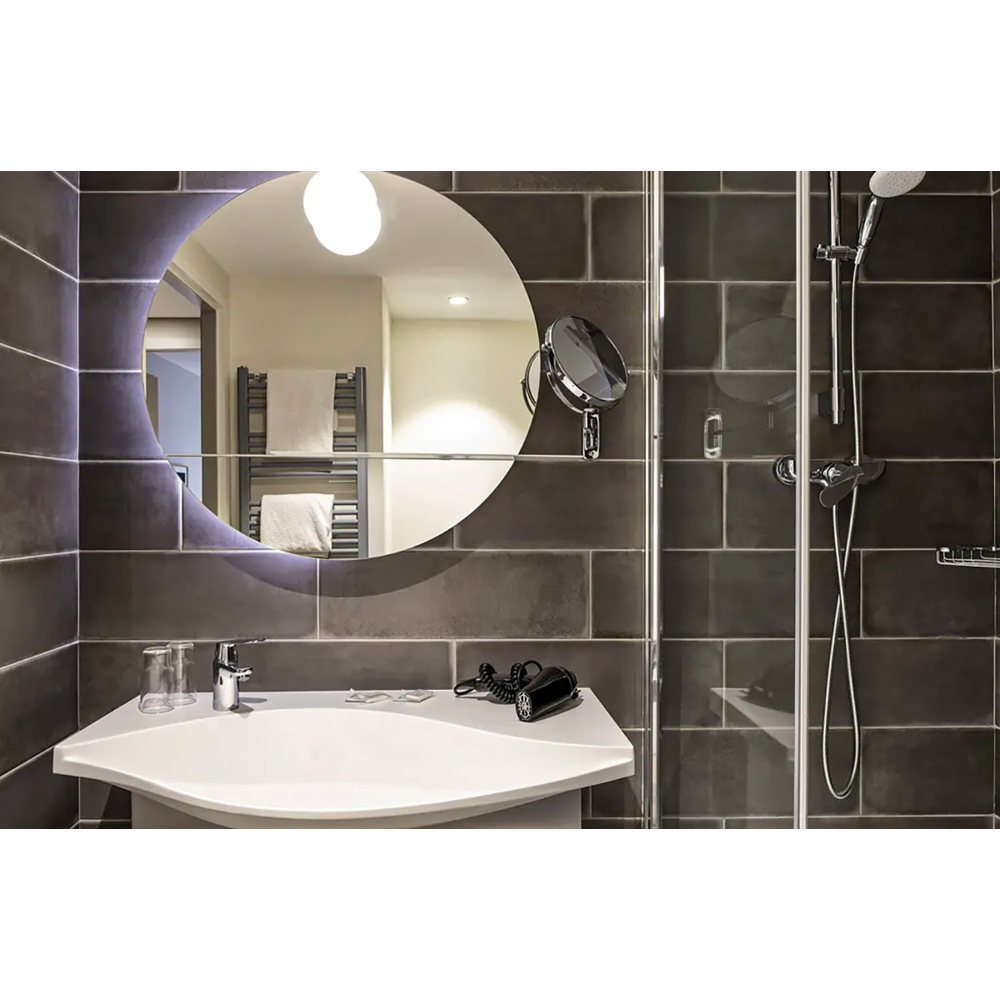 Modernes Badezimmer mit weißem Waschbecken, runden Spiegel und dunklen Fliesen.