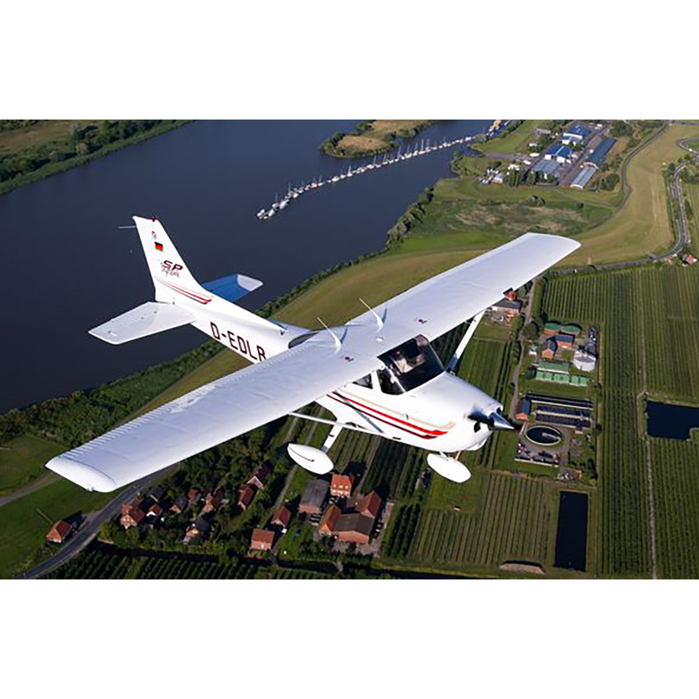Ein kleines weißes Flugzeug fliegt über eine grüne Landschaft mit Feldern und einem Fluss.