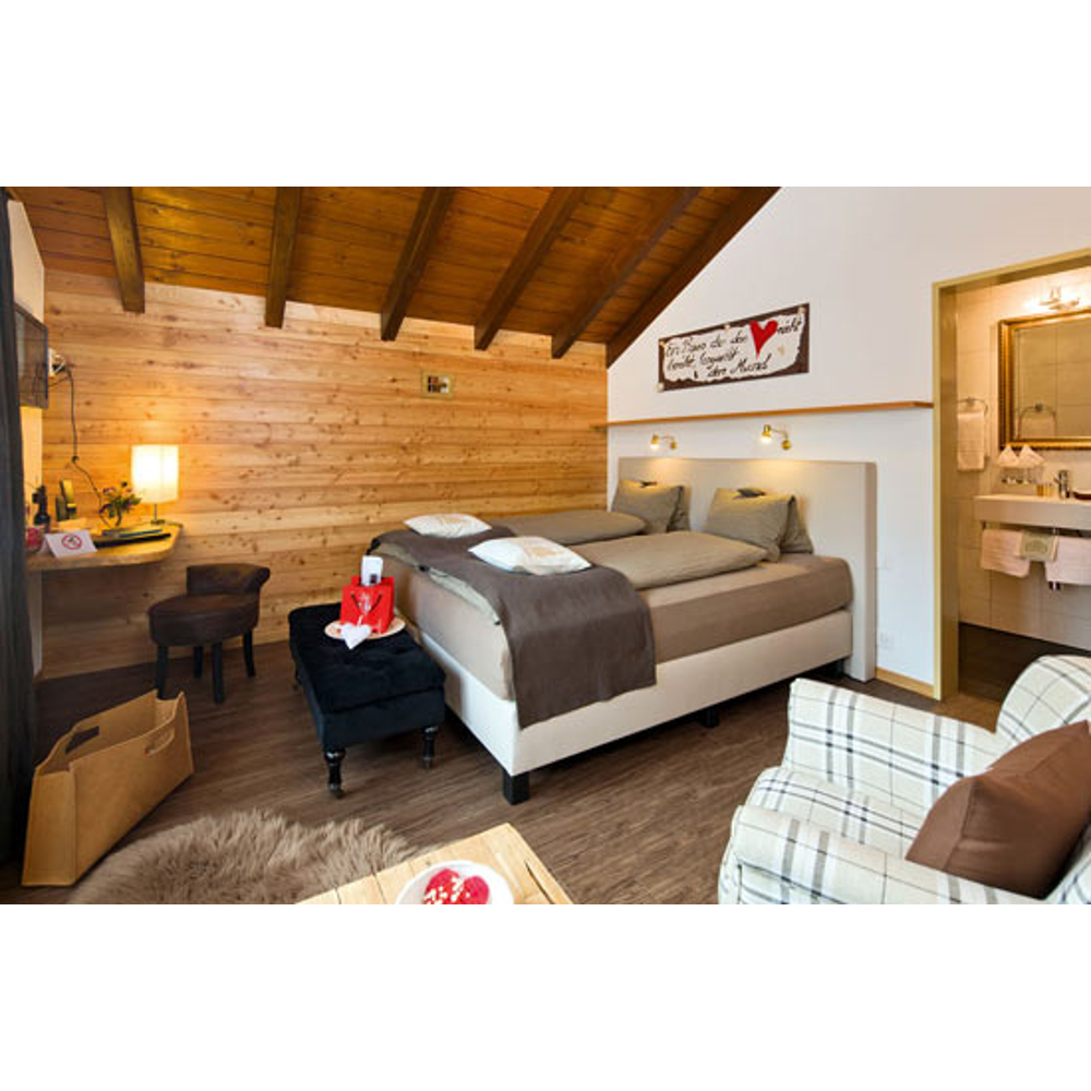 Gemütliches Schlafzimmer mit Holzverkleidung, großem Bett, Plaid-Sessel und offener Badezimmertür.
