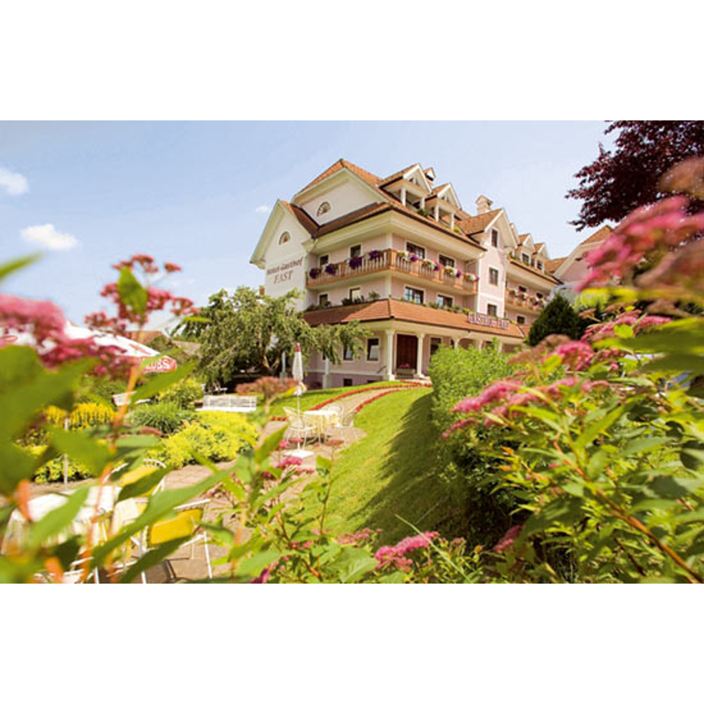 Rosa Hotel mit Blumen im Vordergrund und Grünanlagen.
