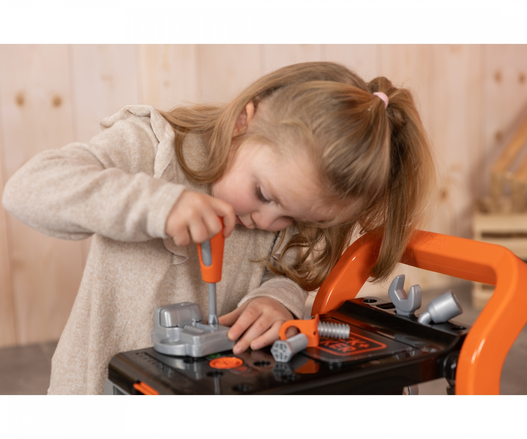 Ein kleines Mädchen mit einem Dutt spielt mit einem orangen und schwarzen Spielzeug-Werkbank.