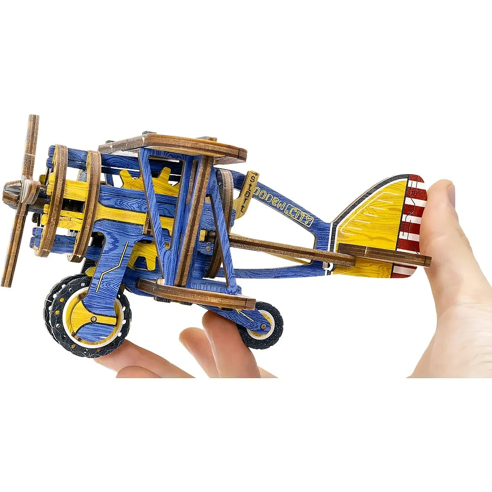 Eine Hand hält ein blau-gelbes Holzmodell eines Doppeldecker-Flugzeugs auf weißem Hintergrund.