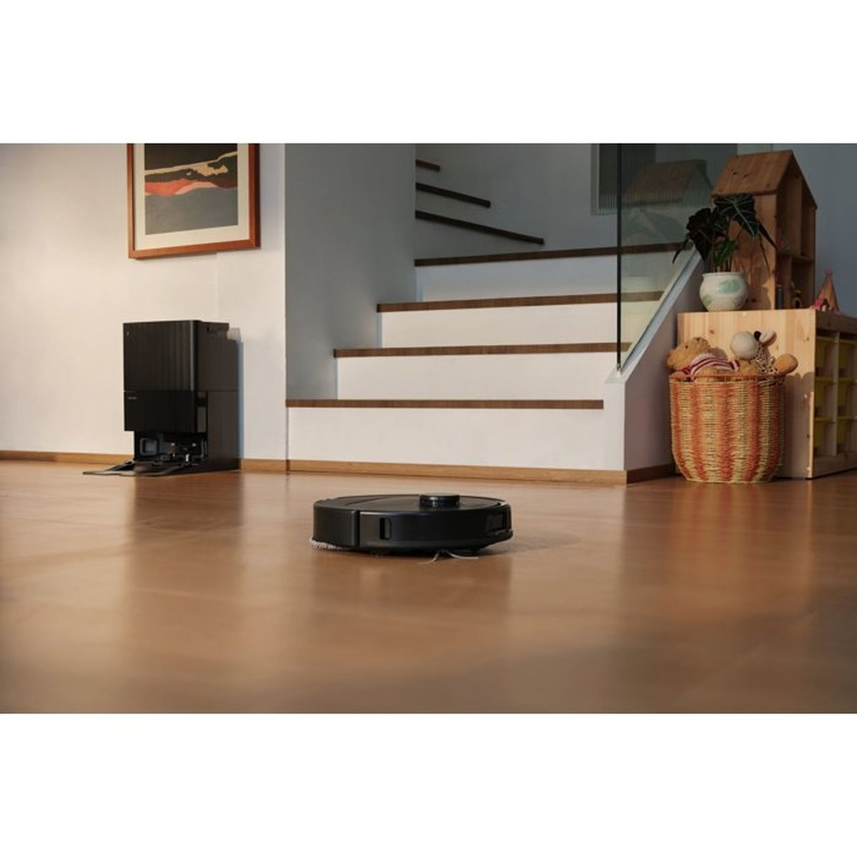 Un robot aspirapolvere nero si muove su un pavimento in legno in un soggiorno vicino alle scale.