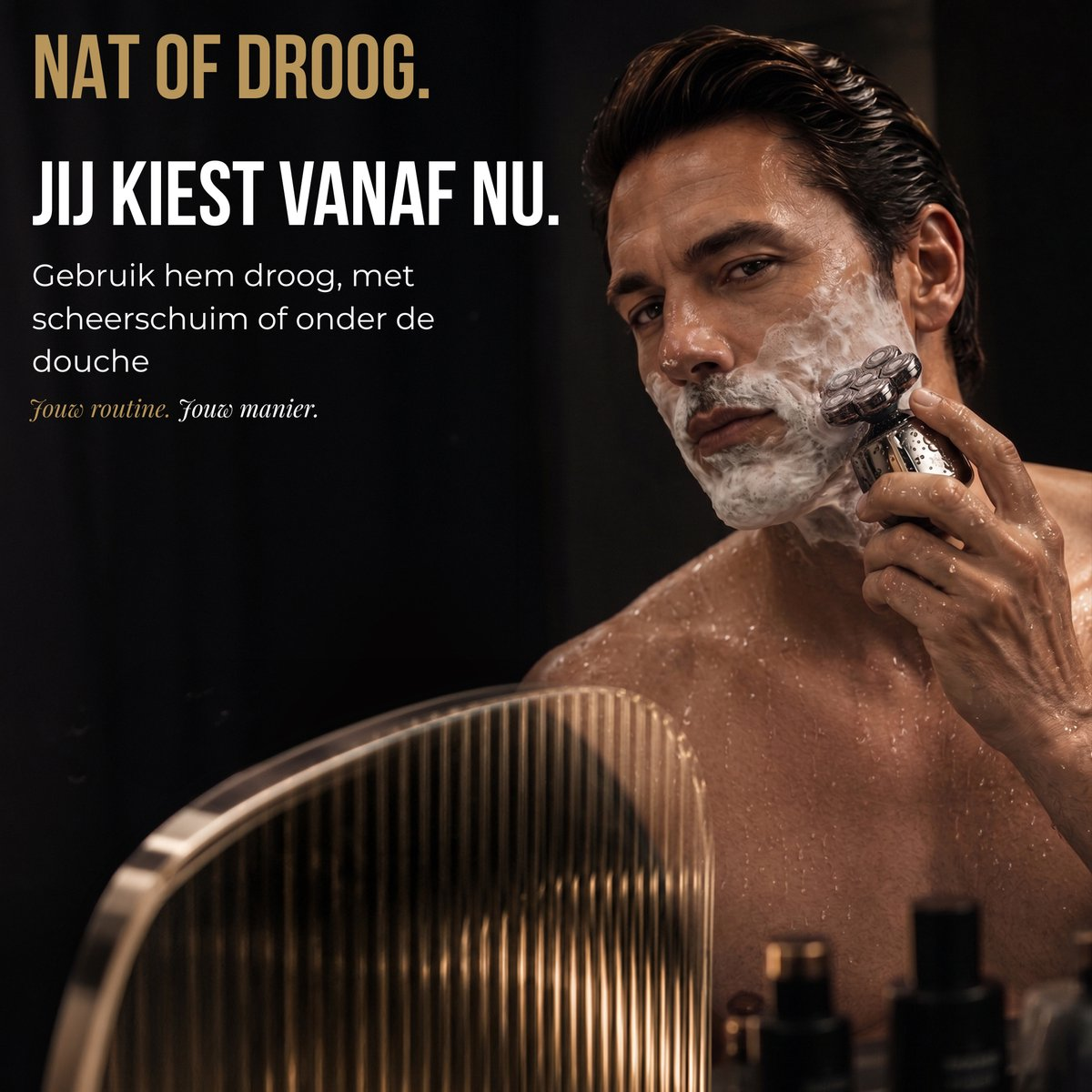 A man with shaving foam on his face shaves with an electric razor in front of a mirror.