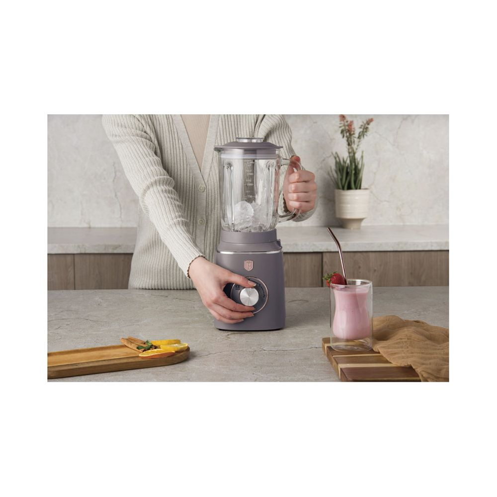 Personne utilisant un mixeur gris sur un comptoir avec une boisson aux fruits et des accessoires.