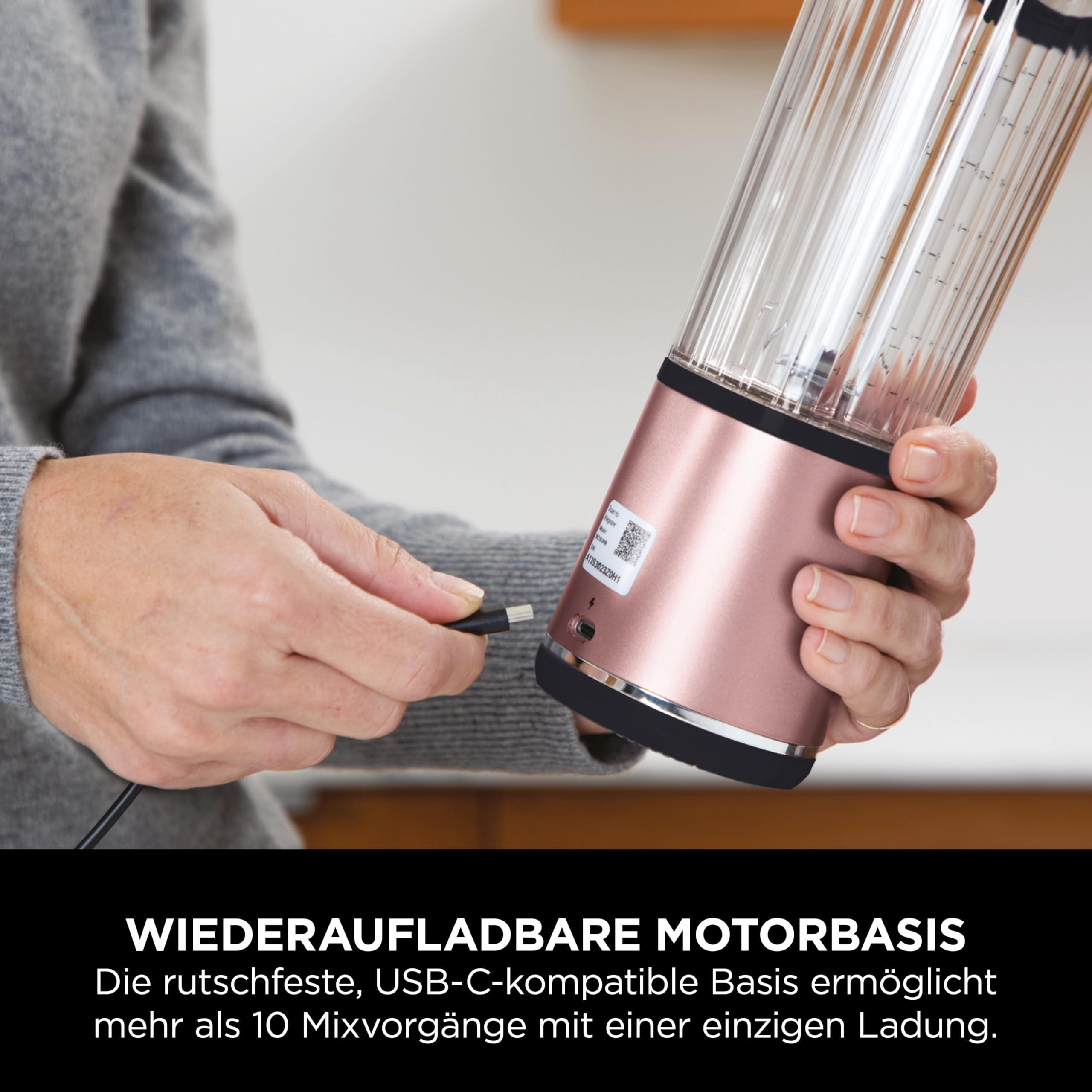 Eine Person verbindet ein USB-C-Kabel mit einer wiederaufladbaren, roséfarbenen Mixerbasis.