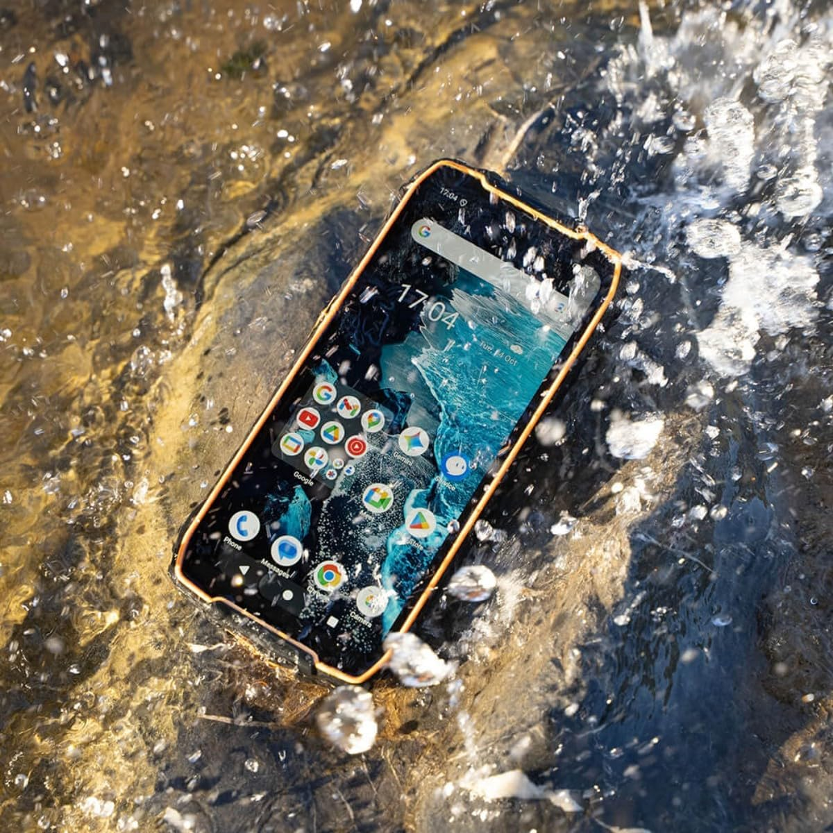 Ein robustes Smartphone mit orangefarbenem Rahmen liegt im fließenden Wasser, bespritzt von Wassertropfen.