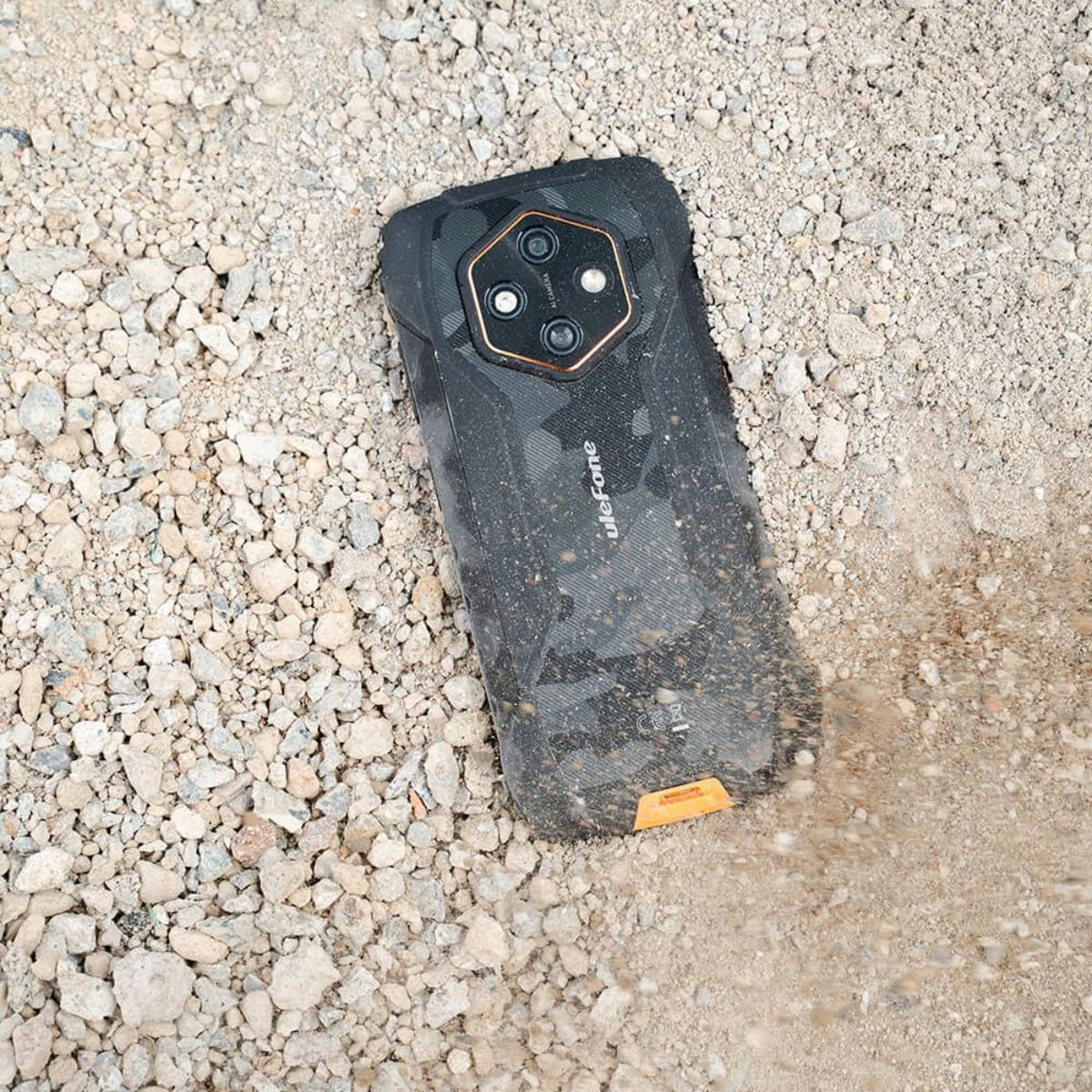 Ein Ulefone-Smartphone liegt auf einem staubigen Kiesboden, besprüht mit Sand.