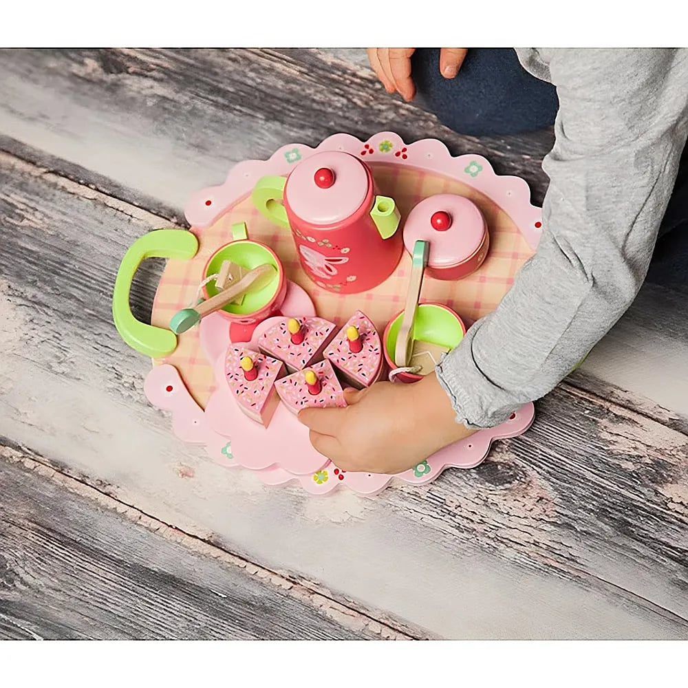 Un enfant joue avec un service  à thé rose et des parts de gâteau sur un plateau en bois.