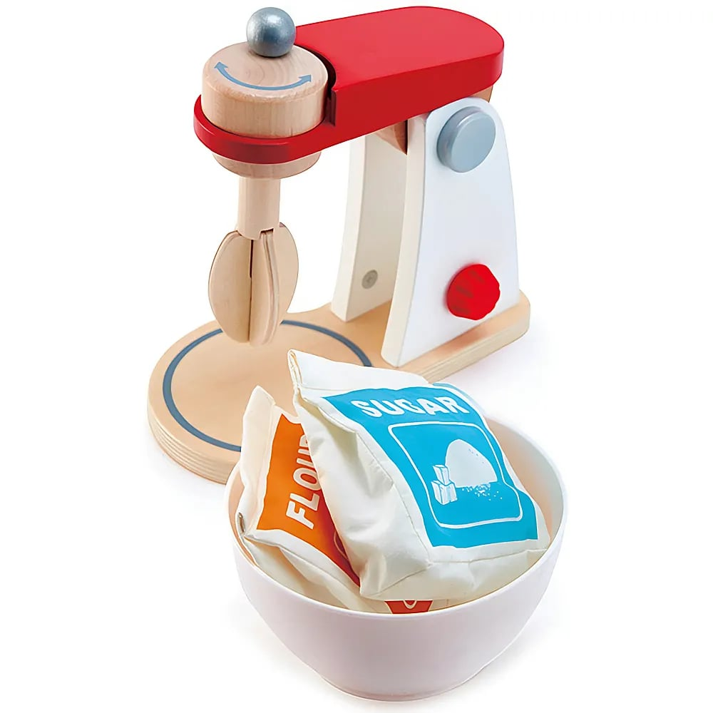 Ein hölzernes Spielzeug-Mixgerät mit roten und weißen Teilen steht hinter einer Schüssel mit Mehl- und Zuckertüten.