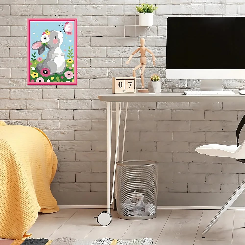 Ein Schreibtisch mit Computer und ein Hasenbild an einer Ziegelwand.