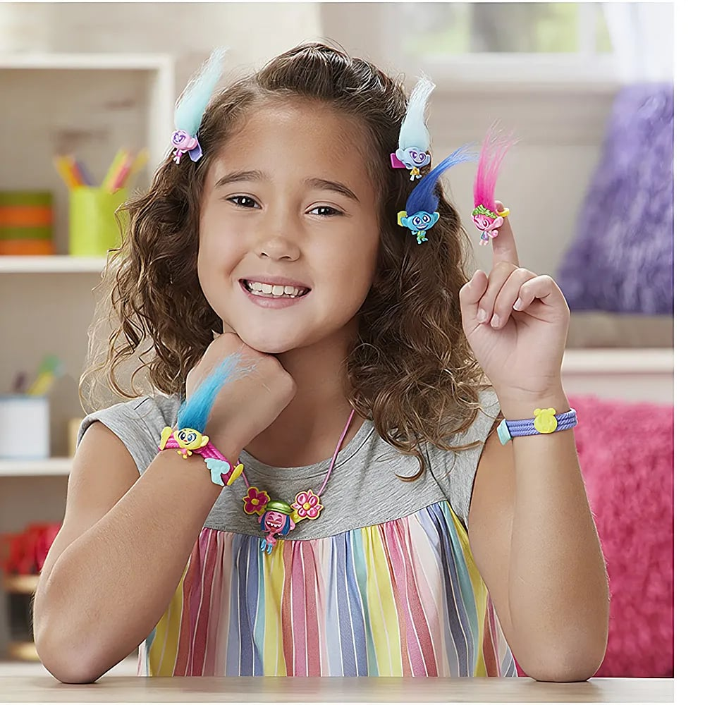 Une fille souriante porte des pinces à cheveux, des bracelets, un collier et une bague Trolls.