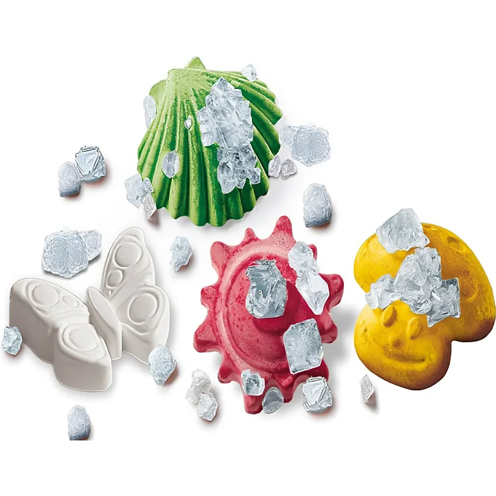 Bunte Tonformen von Muscheln, Schmetterlingen und Gesichtern mit kristallinen Salzbrocken auf weißem Grund.
