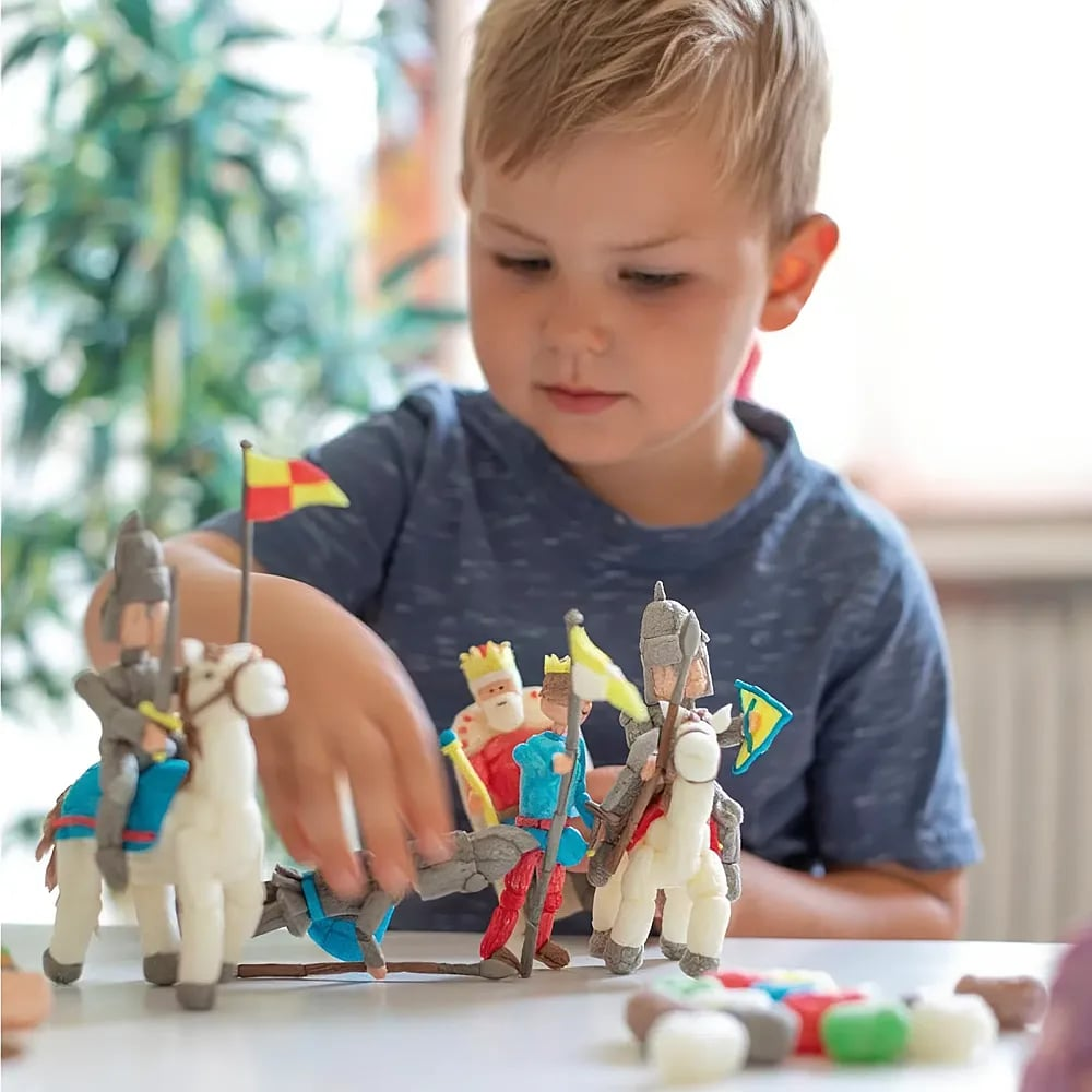Ein Junge spielt an einem Tisch mit selbstgemachten Tonfiguren von Rittern und Pferden.