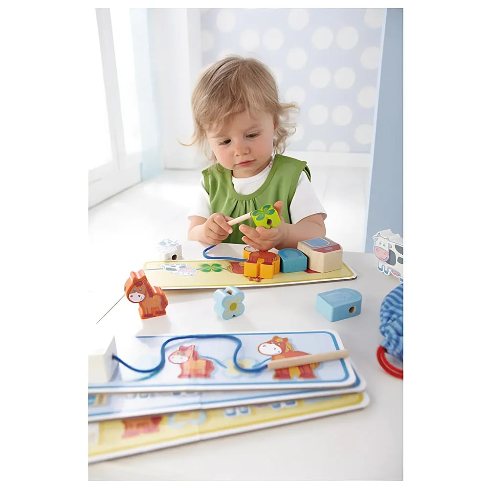 Un tout-petit assis à une table joue avec des jouets à lacer en bois colorés devant un mur à pois bleus.