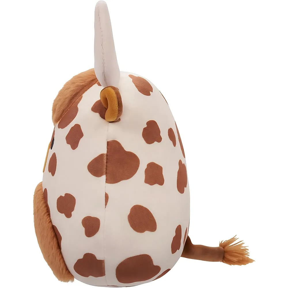 Une vache en peluche avec des taches brunes, une corne blanche et une queue poilue, vue de profil.