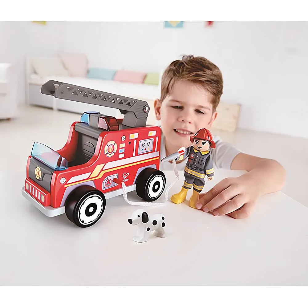 Un niño juega con un camión de bomberos de juguete rojo, una figura de bombero y un perro dálmata.