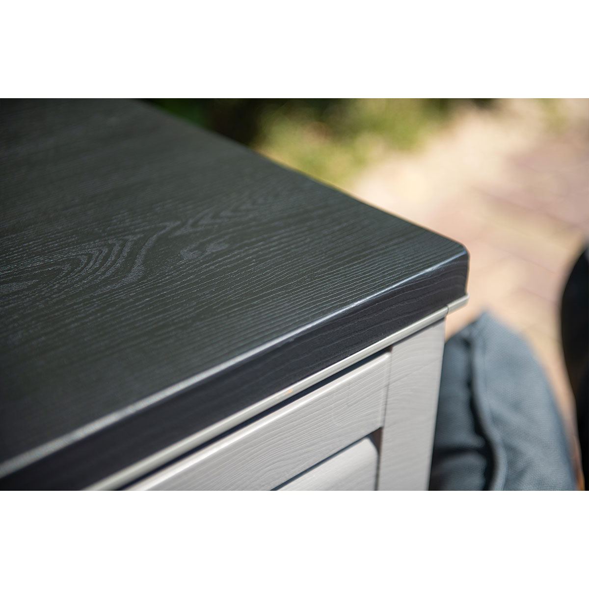 Close-up of a dark, wood-grained tabletop on a gray frame outdoors.