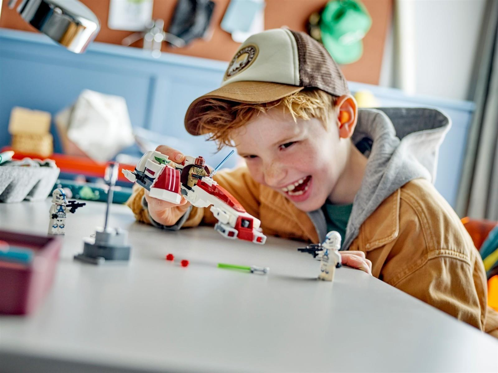 Ein glücklicher Junge spielt am Tisch mit Star Wars LEGO-Figuren und einem Raumschiff.