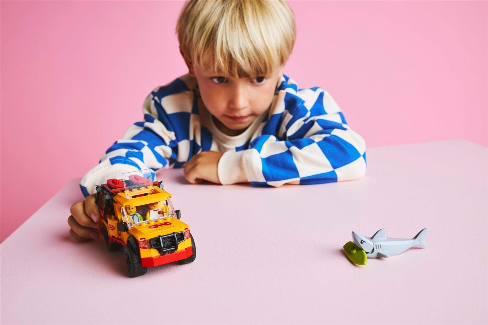 Ein kleiner blonder Junge in einem blau-weiß karierten Hemd spielt mit einem gelben Spielzeugauto und einem Hai.