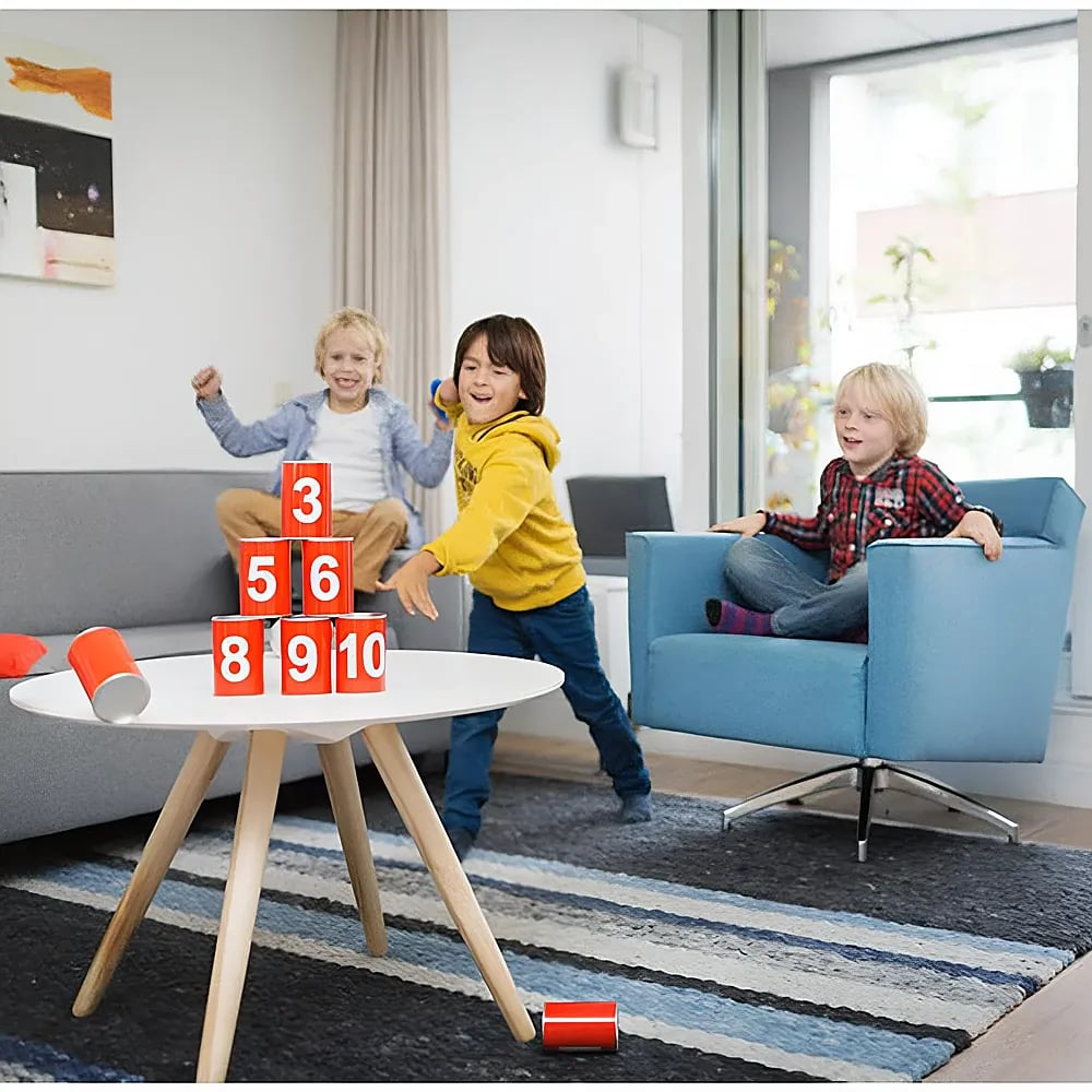 Drei Kinder spielen in einem Wohnzimmer, werfen Dosen mit Nummern auf einem Tisch um.