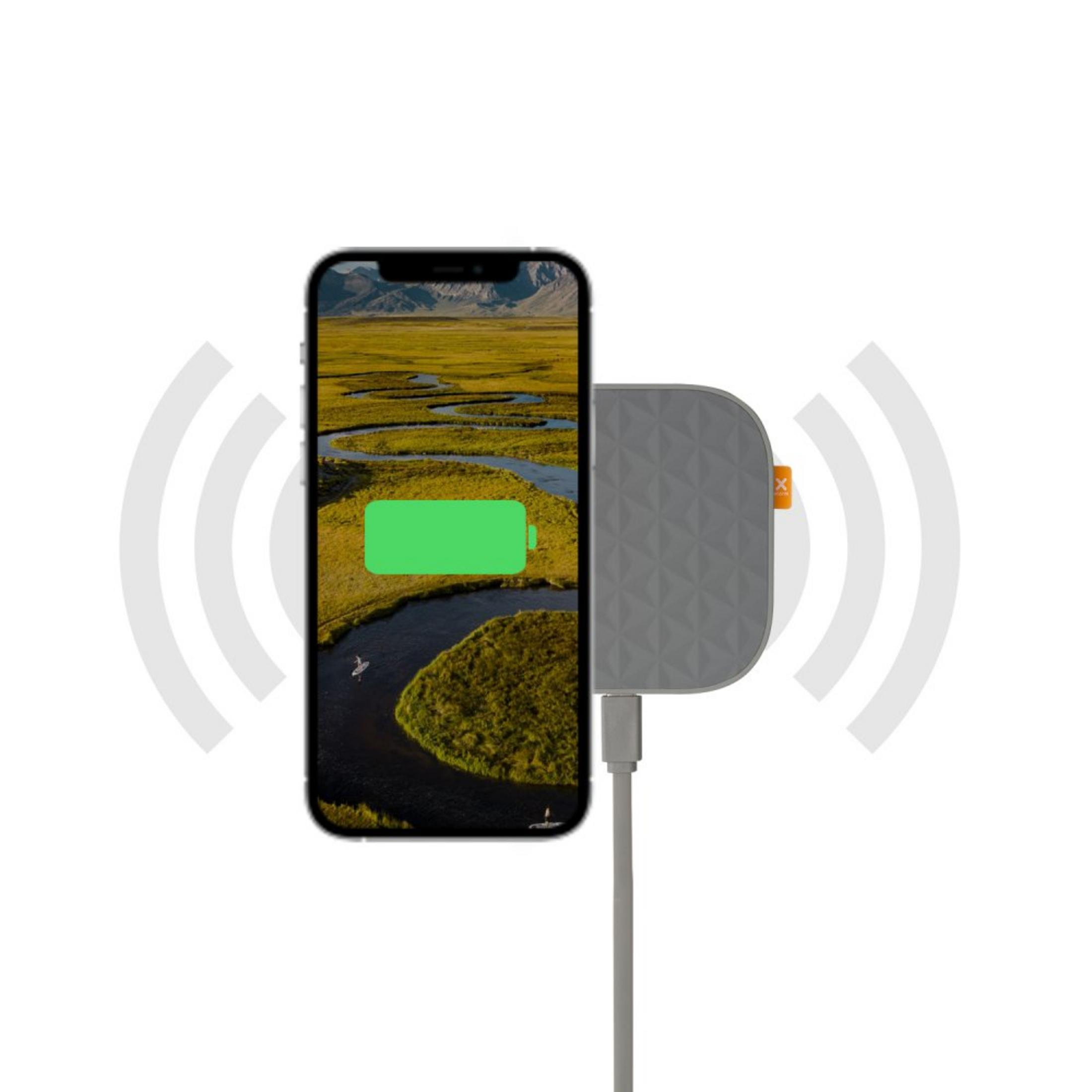 Ein Smartphone lädt kabellos auf einem grauen Pad mit Landschaftshintergrund und sendet Signalwellen aus.