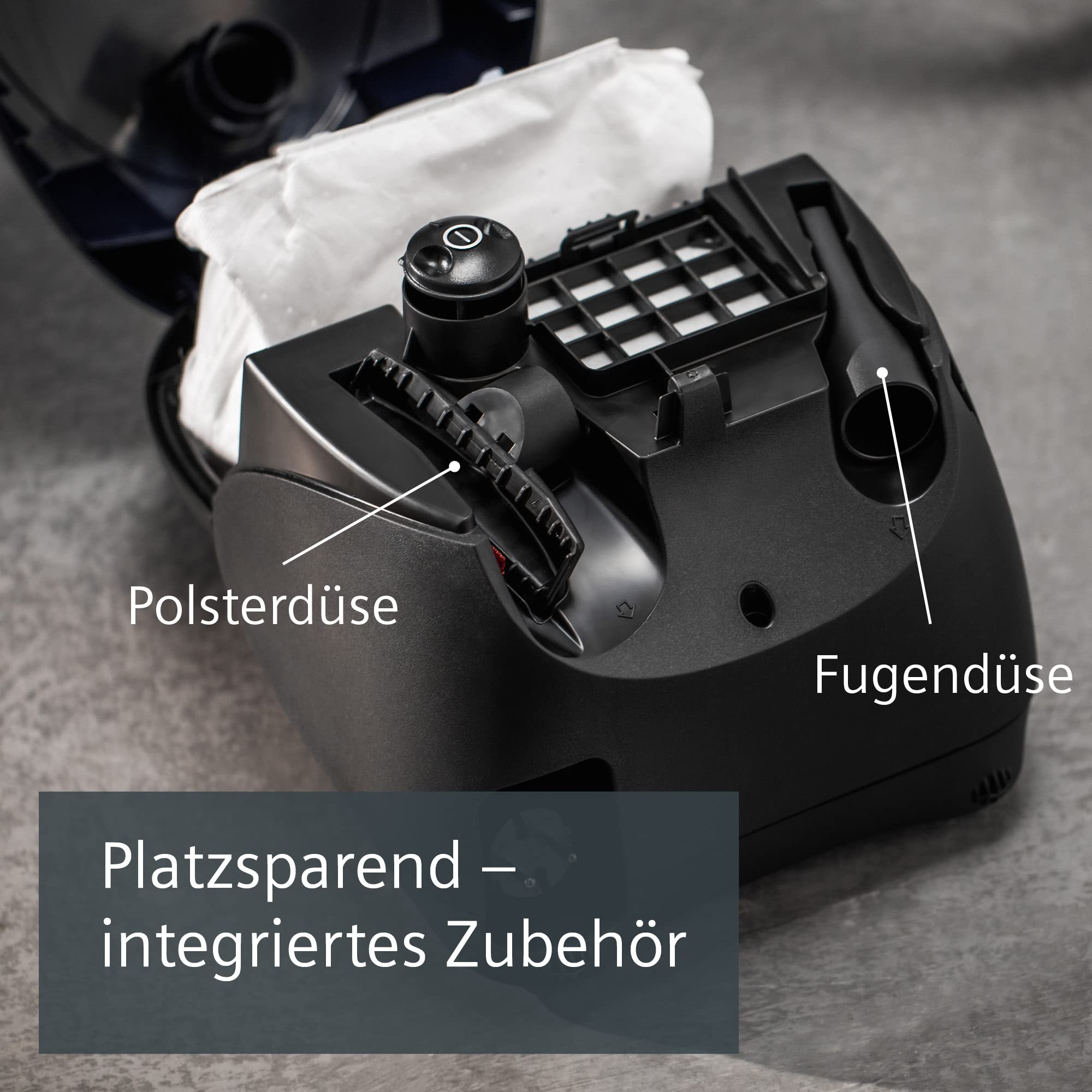 Aspirapolvere nero aperto con accessori integrati, filtro e sacchetto su superficie grigia.