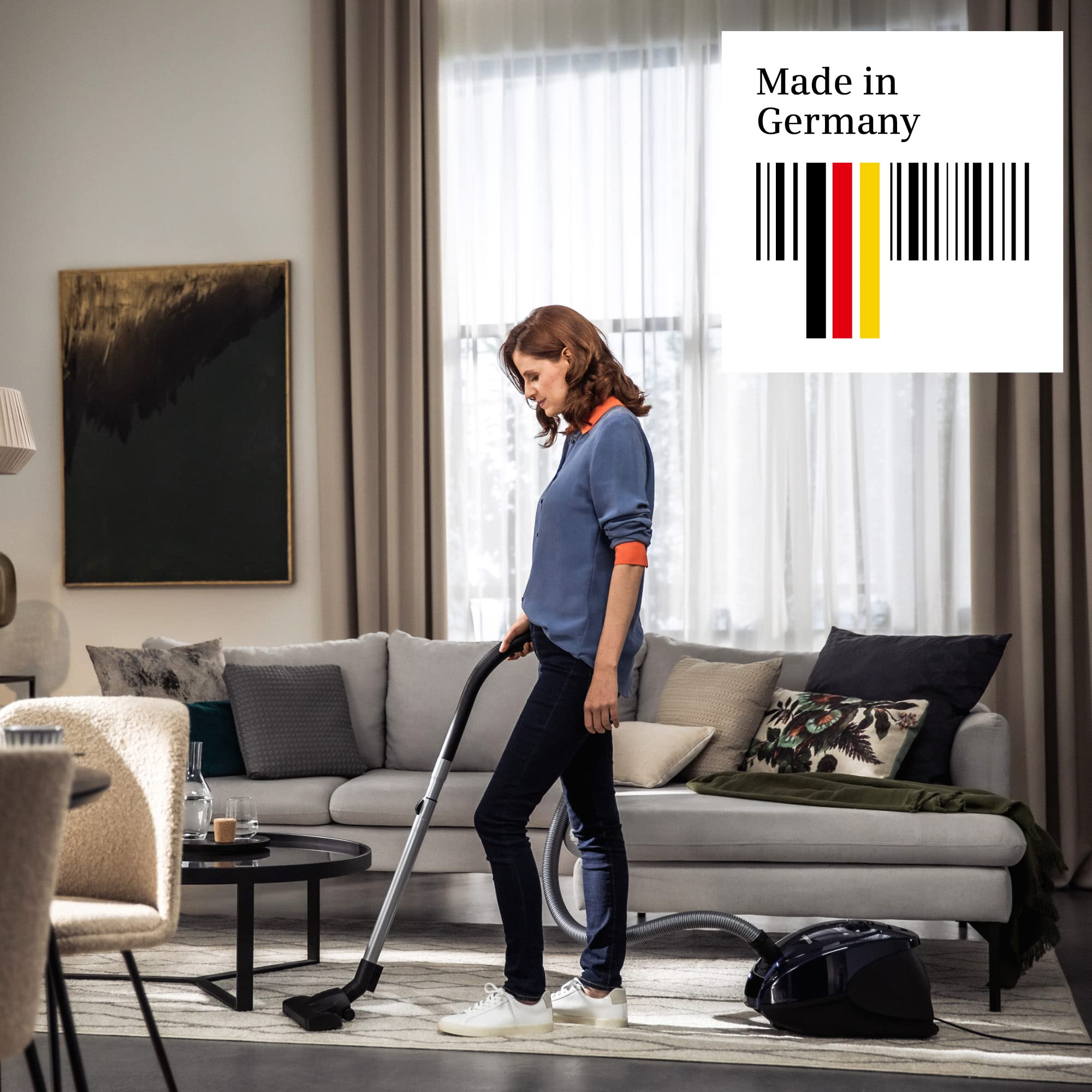 Donna aspira tappeto in luminoso soggiorno con divano; logo "Made in Germany".